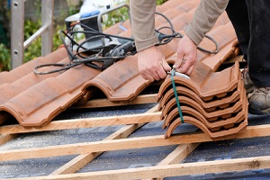 construction worker on a renovation roof covering it with tiles using hammer