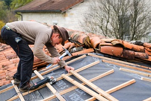 construction worker on a renovation roof covering it with tiles using hammer