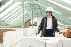 woman architect checking blueprints against wooden roof framing of modern farmhouse